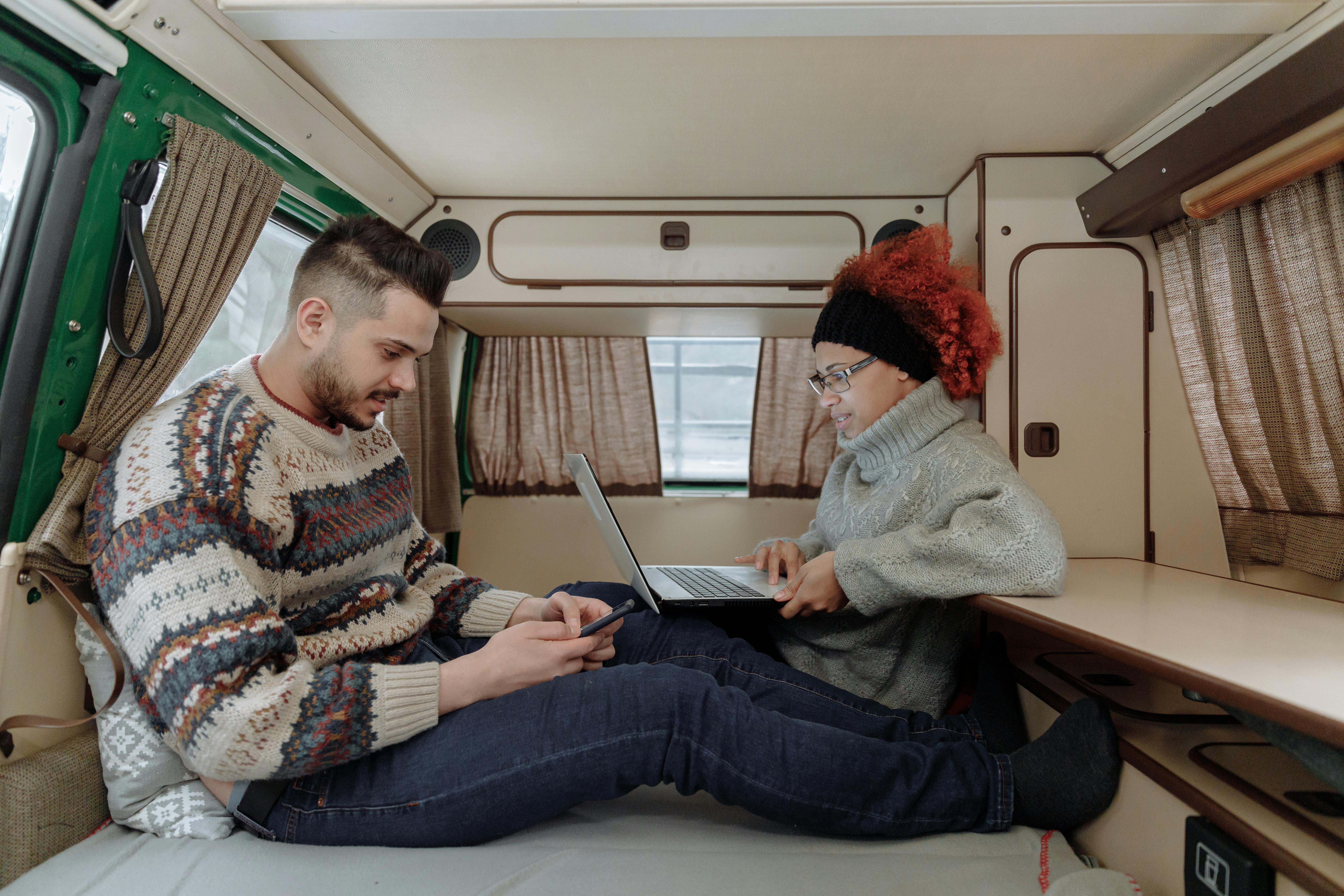 Couple using a smartphone and laptop inside a camper van, embracing the digital nomad lifestyle.