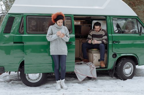 Free A couple enjoying a cozy winter moment outside their green van amidst snowy surroundings. Stock Photo