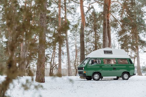 Free Explore the tranquil beauty of winter with a classic green camper van parked in a snowy forest. Stock Photo