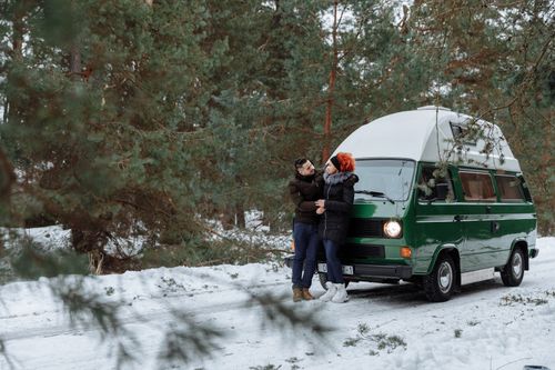 Free A couple enjoys a winter trip with their green campervan surrounded by snow and pine trees. Stock Photo