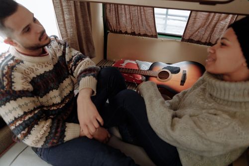 Free A couple enjoying a cozy moment inside a camper van, with a guitar and warm sweaters. Stock Photo