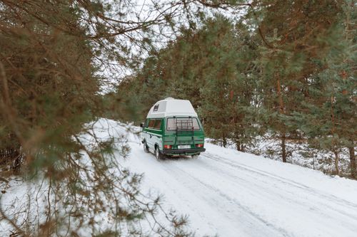 Free Green camper van driving on a snowy forest road during winter, capturing the spirit of adventure. Stock Photo