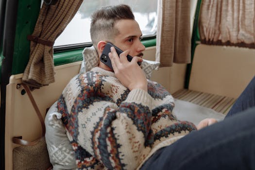 Casual adult man wearing sweater, relaxing indoors while talking on phone.