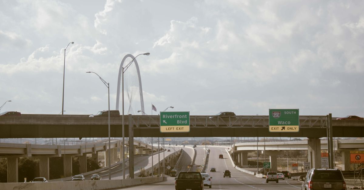 Daytime view of a busy expressway in Dallas, Texas featuring cars and road signs.