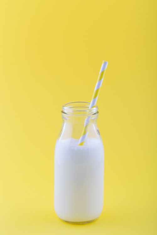 Free Milk in a clear glass jar with a striped straw against a yellow background. Stock Photo