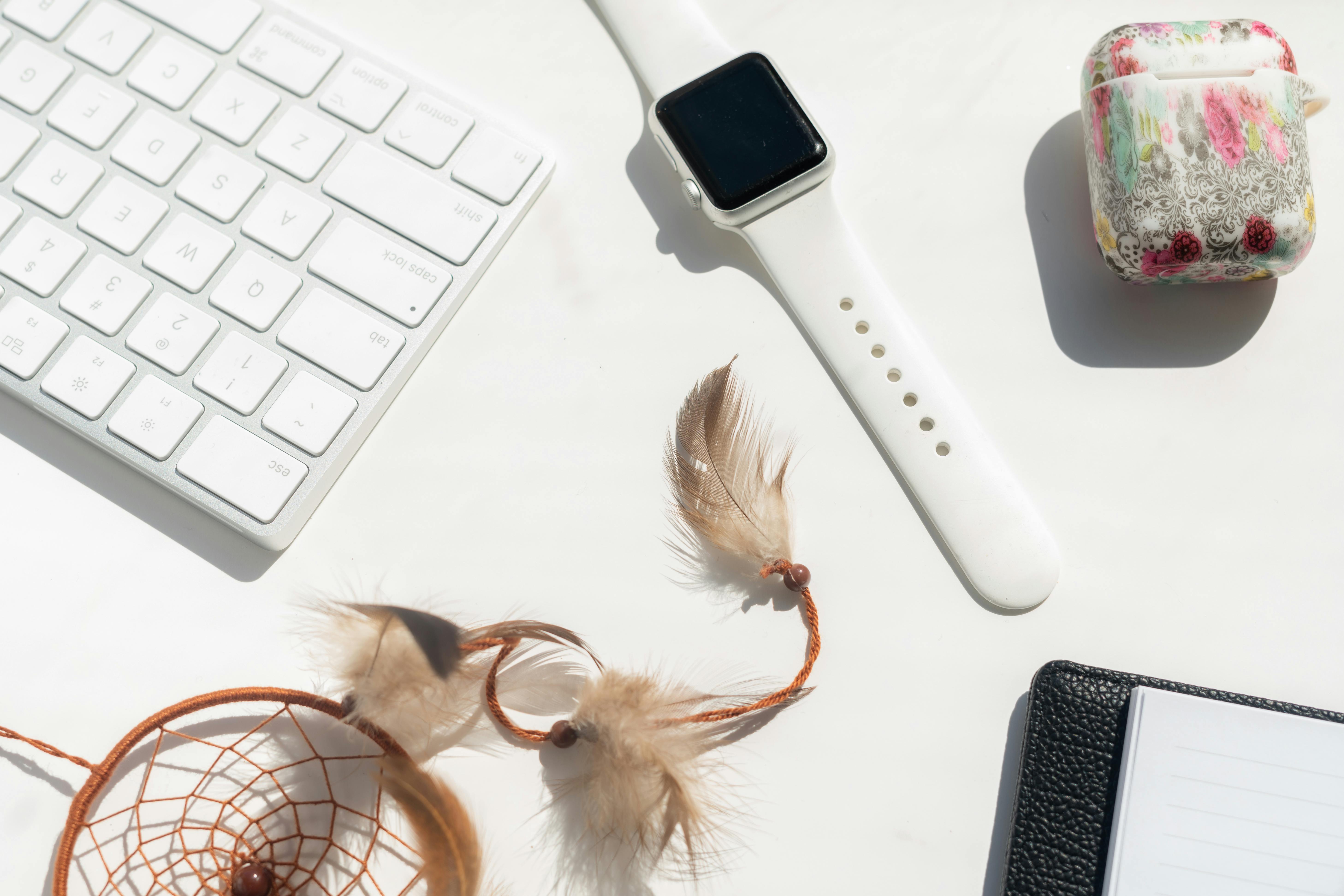 Flat lay of a modern workspace featuring a smartwatch, keyboard, and decorative items on a white background.