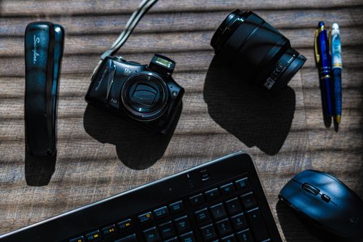 Flat lay of office essentials including a camera, keyboard, and lens on a wooden desk.