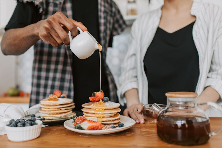 
A Person Pouring Maple Syrup On A Stack Of Pancakes