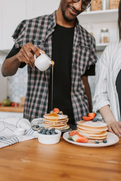 Free A man pouring syrup over pancakes topped with fresh berries, creating a delicious breakfast scene. Stock Photo