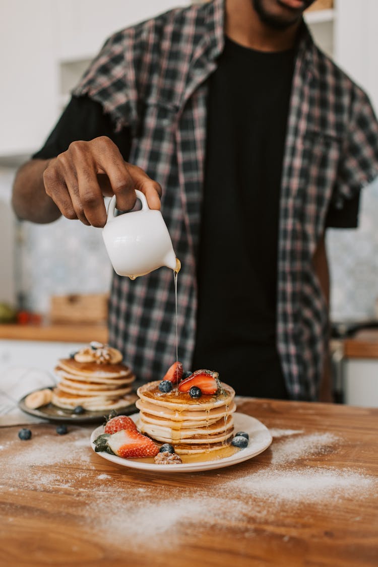 A Person Pouring Maple Syrup On A Stack Of Pancakes