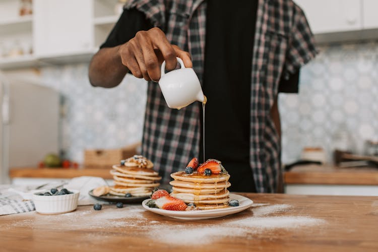 A Person Pouring Maple Syrup On A Stack Of Pancakes