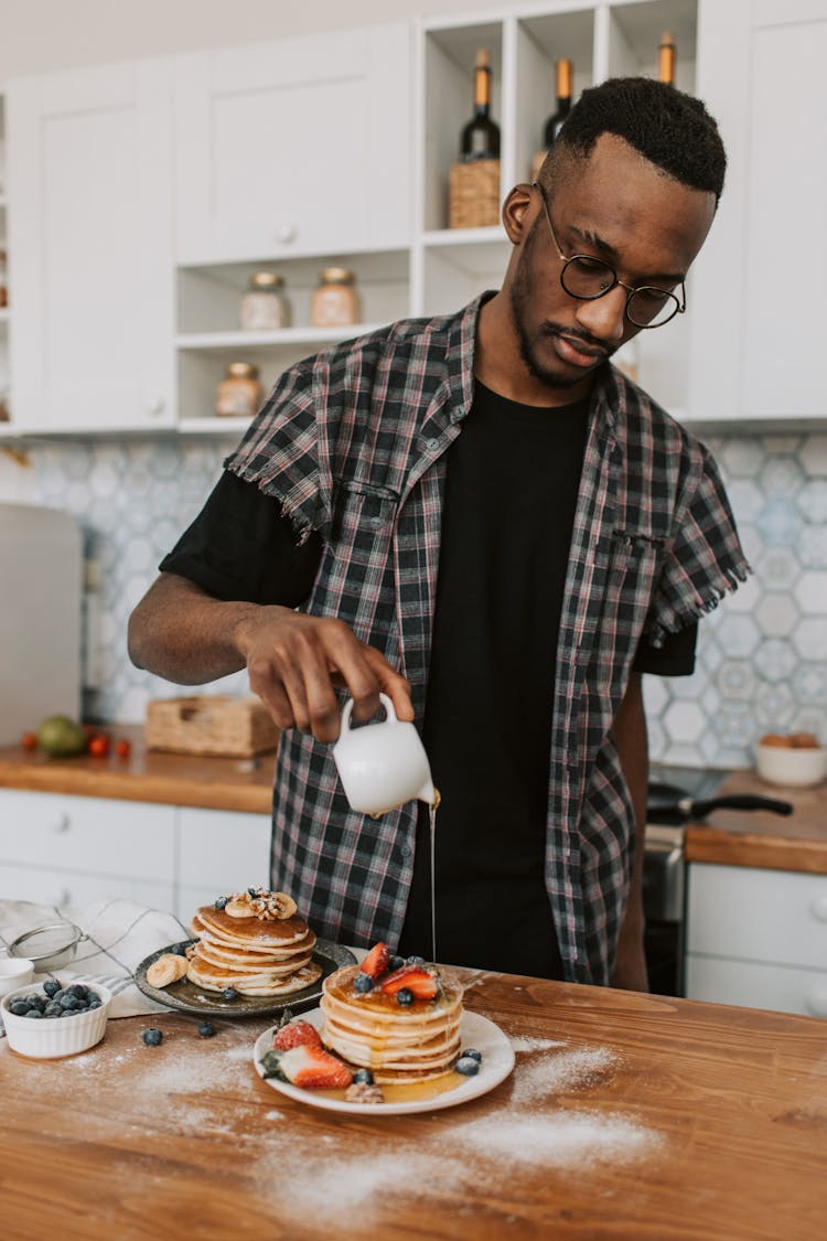 A Man Pouring Maple Syrup On A Stack Of Pancakes