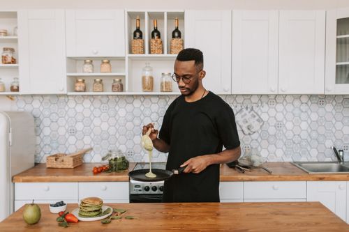 Free A man pours batter while preparing pancakes in a stylish kitchen. Delicious breakfast scene. Stock Photo