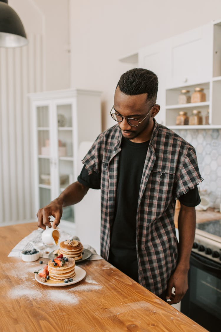 Person Wearing Eyeglasses Pouring Syrup On Pancakes