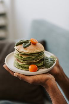 Close-up of green spinach pancakes garnished with tomatoes, held on a white plate.