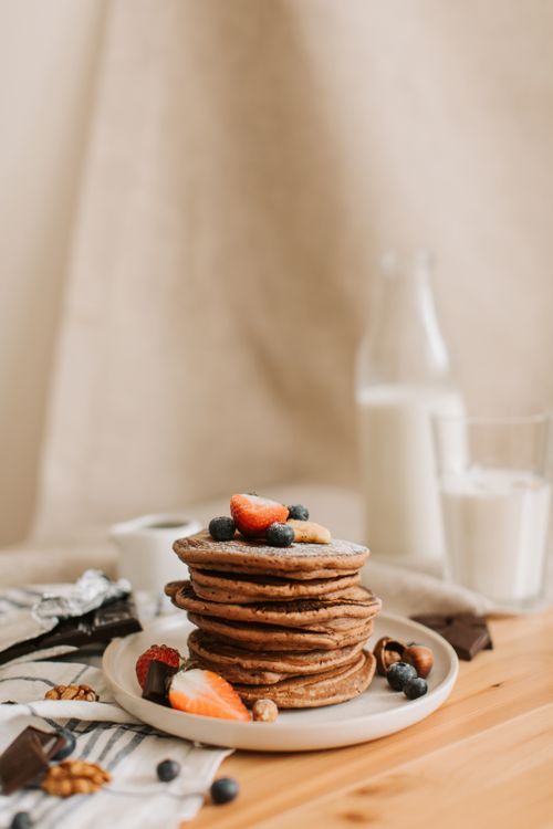 Free Delicious stack of pancakes topped with fresh berries and served with milk on a wooden table. Stock Photo