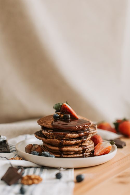 Free Stack of chocolate pancakes topped with strawberries and blueberries, drizzled with syrup. Stock Photo