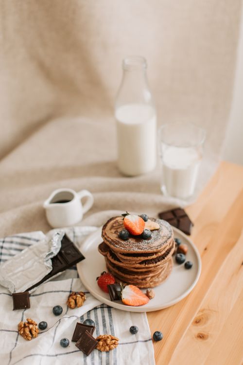 Free Appetizing pancake stack with berries, walnuts, milk, and chocolate on a cozy breakfast setup. Stock Photo