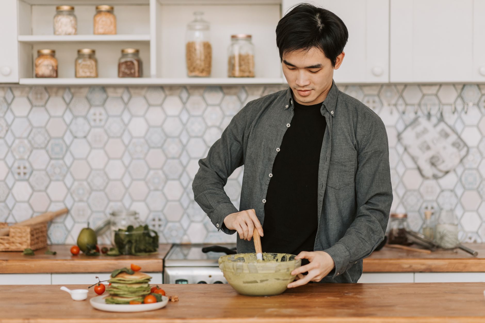 A young man stirs batter in a bowl in a stylish kitchen setting, emphasizing home cooking.