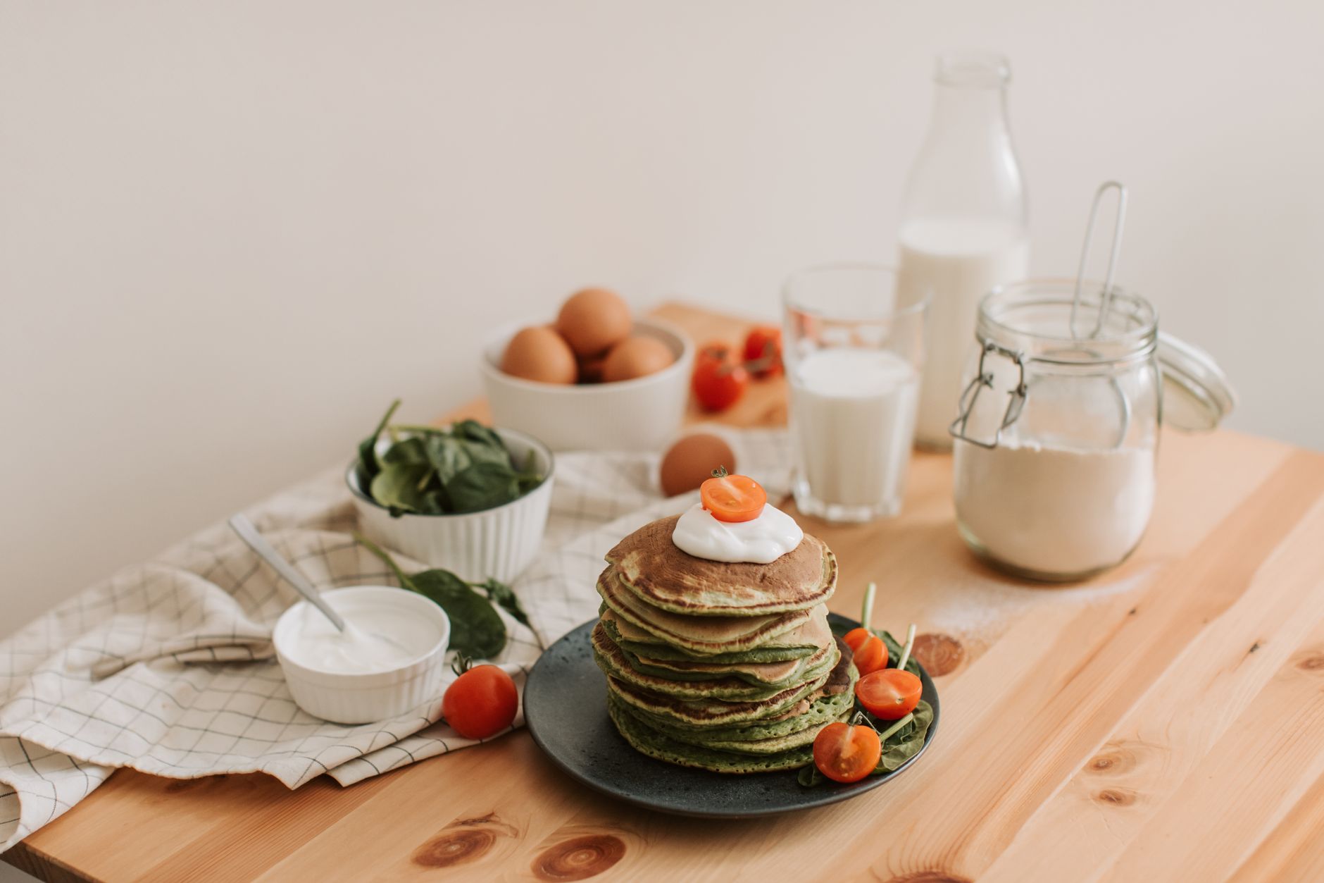 Decadent Creamed Spinach in 25 Minutes for Christmas Delicious stack of pancakes with fresh spinach, tomatoes, eggs, milk, and yogurt on a wooden table.