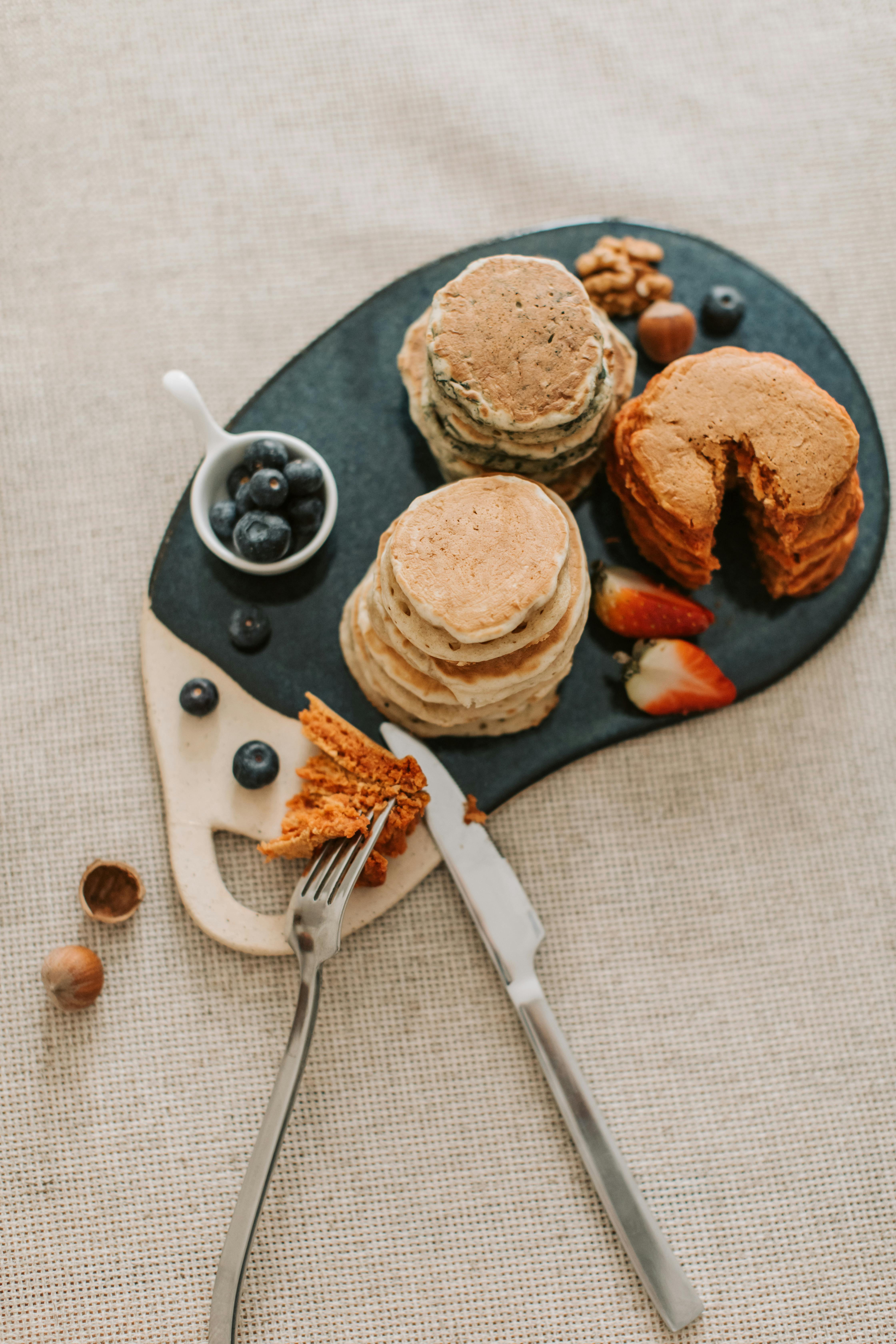 Delicious pancakes stacked with fresh fruits and nuts, artfully arranged on a stylish serving board.