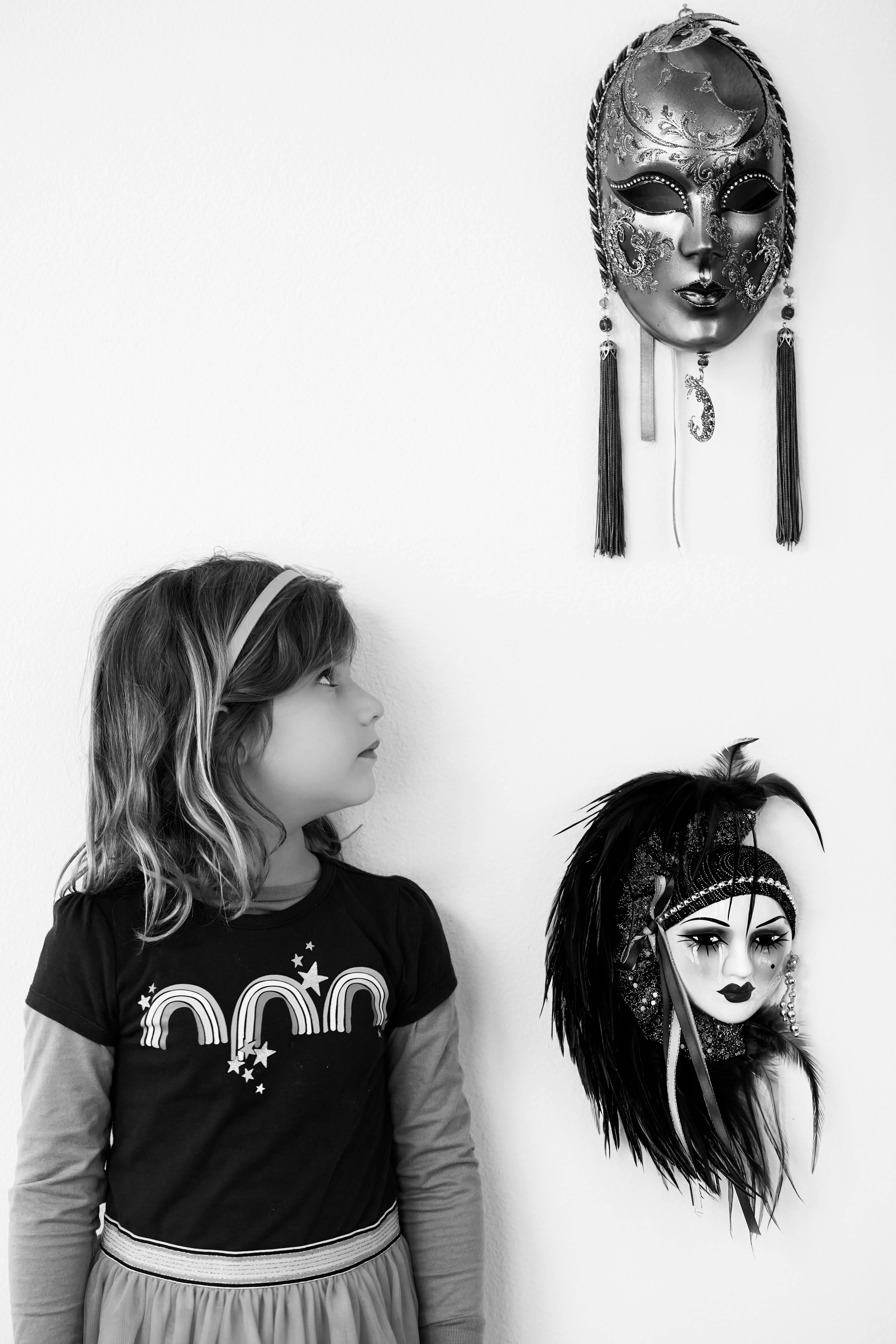 Free Monochrome image of a young girl fascinated by ornate masks displayed on a wall. Stock Photo