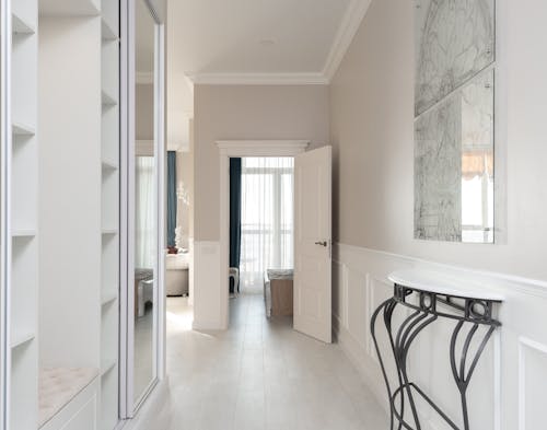 Hallway with empty opened wardrobe and mirror against wall with decorated white shelf in contemporary spacious light flat with rooms