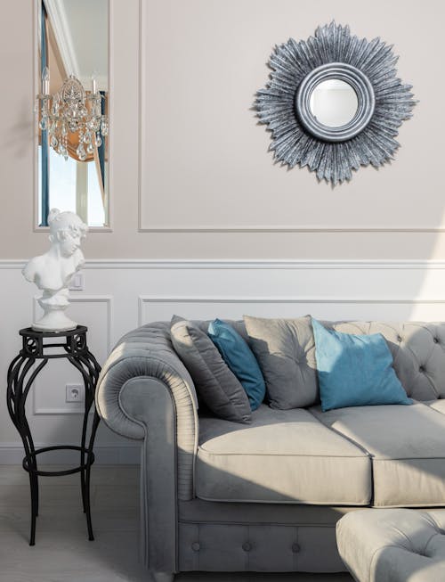 Creative design of living room with decorative bust on table and mirror above couch on sunny day