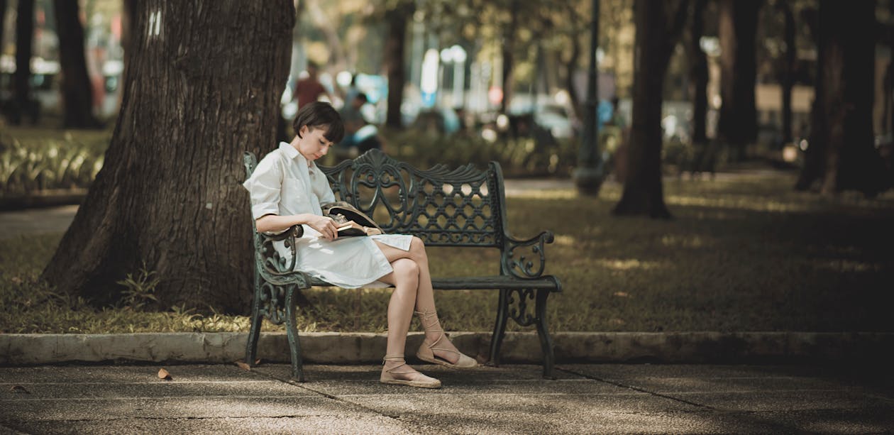 Free Woman Sitting on Metal Bench on Park While Reading Book Stock Photo