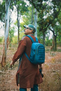 A man with a blue backpack enjoys a hike in a lush forest setting.