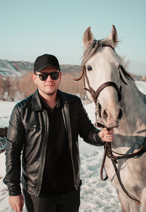 Free A man in a leather jacket and sunglasses stands outdoors holding a white horse. Stock Photo