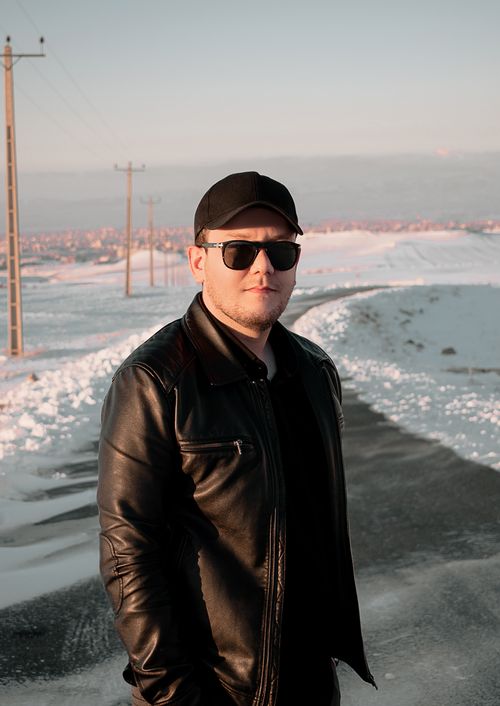 Free A man in sunglasses and a black leather jacket stands on a wintery road with snow-covered landscape. Stock Photo
