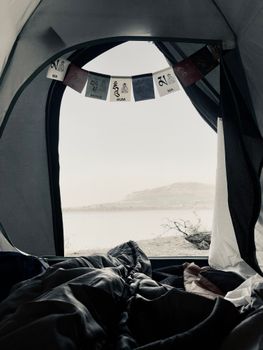 View from inside a tent with hanging flags overlooking mountains and a lake at daytime.