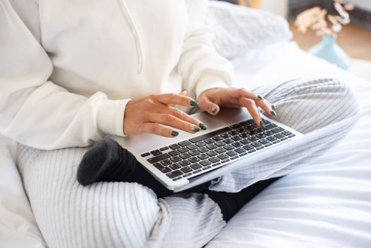 A person in comfortable attire using a laptop while sitting on a bed, working remotely.