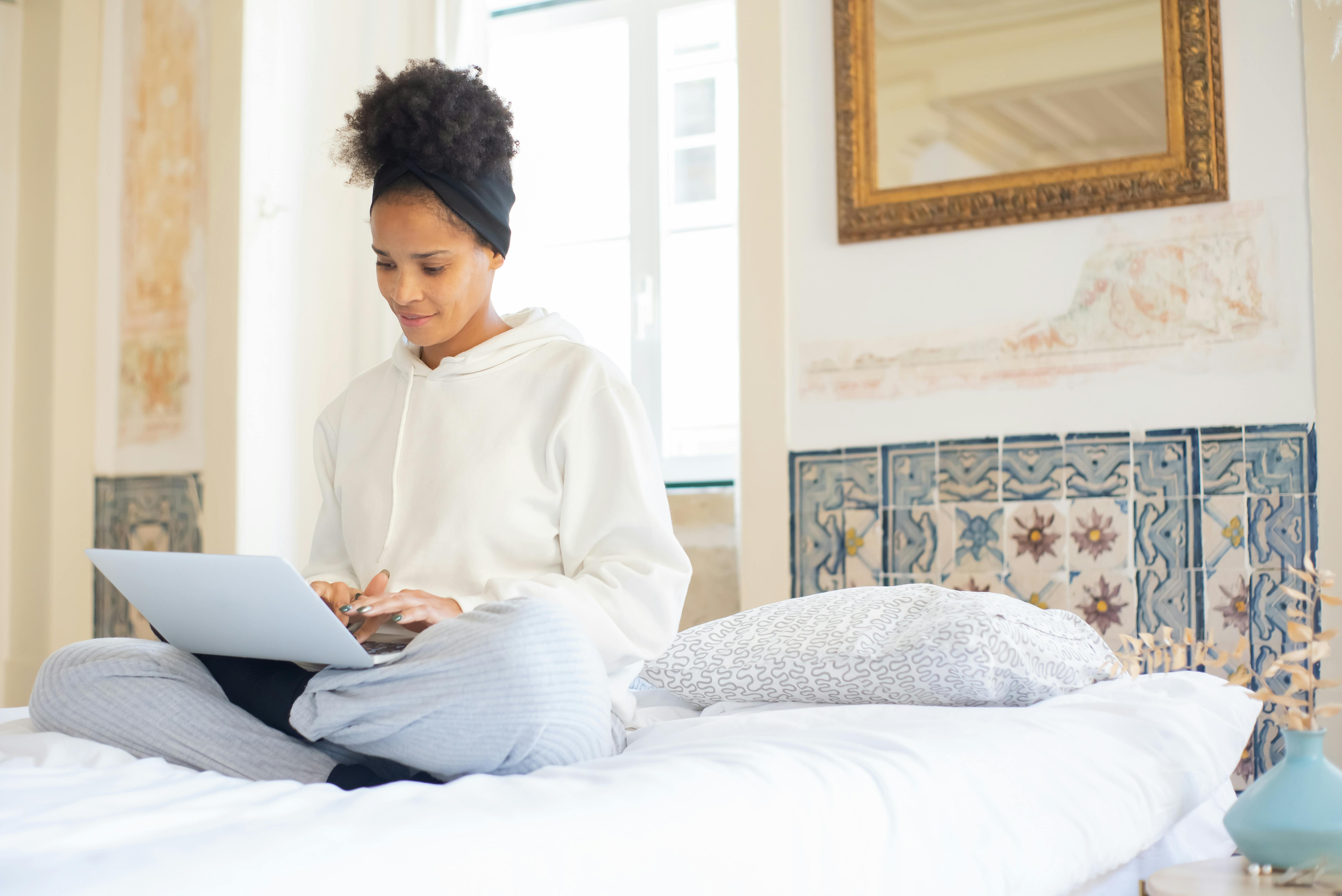 African American woman sitting on a bed using a laptop indoors with decorative tiles in Portugal.