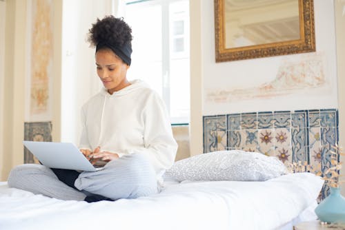 Woman Sitting on Bed While Using a Laptop