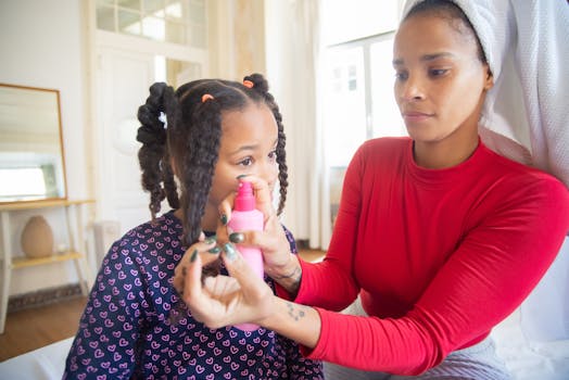 A mother in a red top styles her daughter's hair with a spray bottle. Indoor family moment.