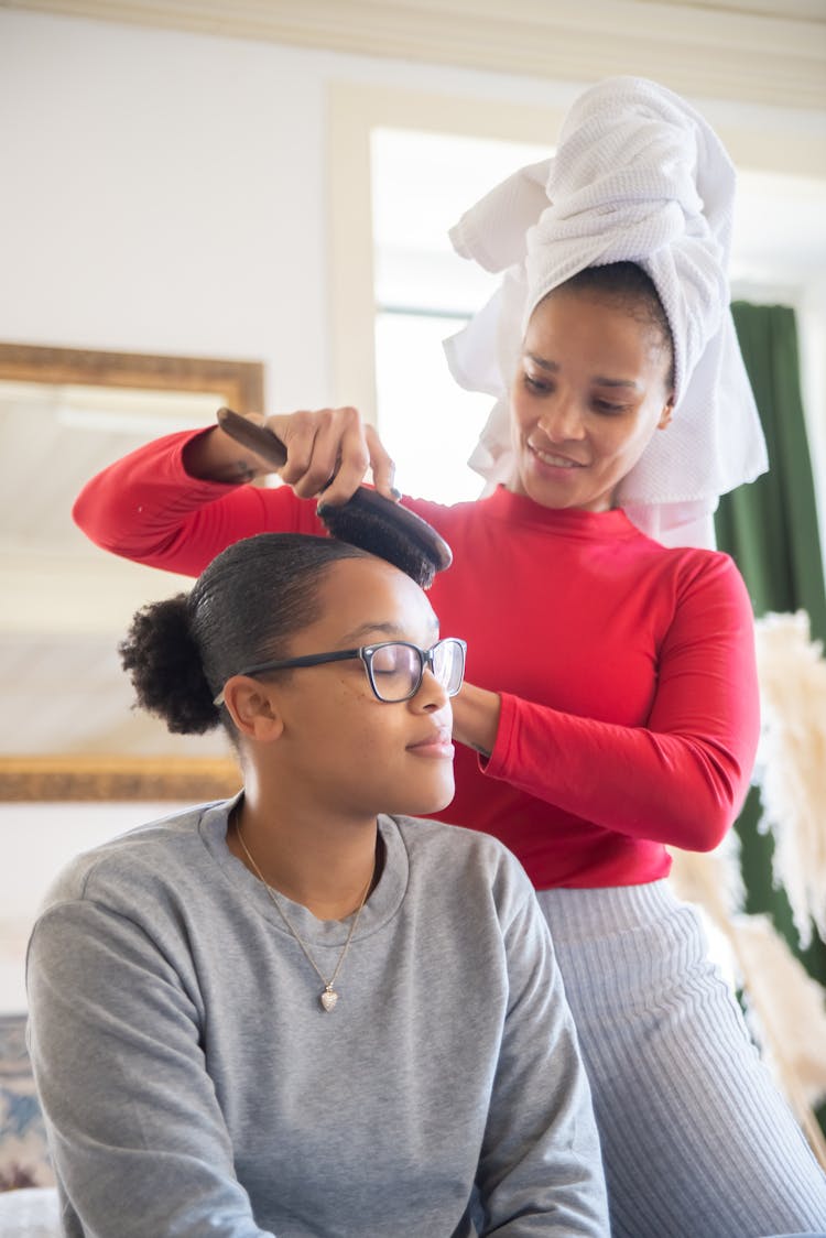 Woman In Red Top Brushing The Hair Of A Girl