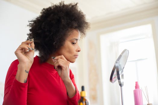A woman with an afro styles her hair in front of a mirror indoors in a well-lit room.