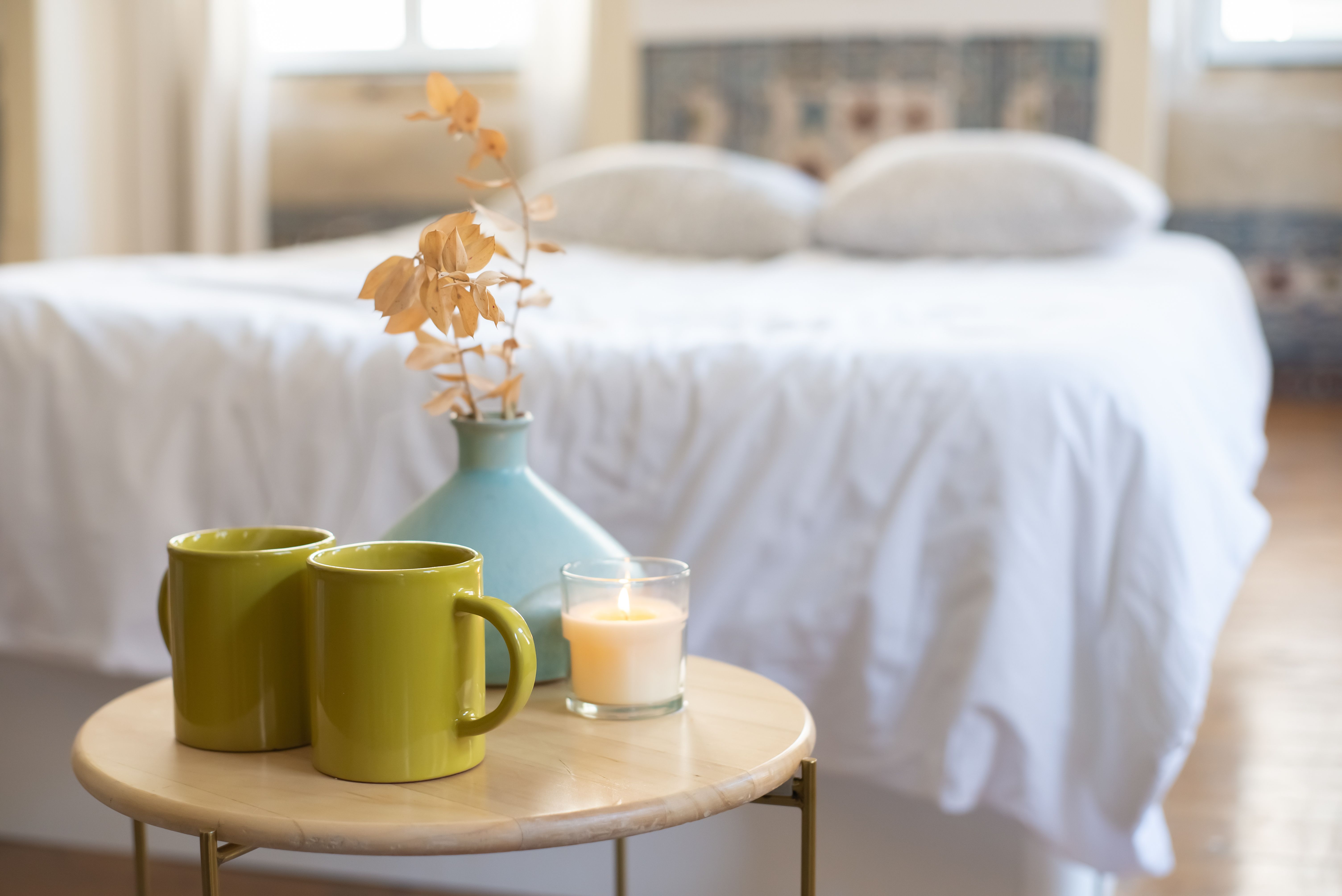 Inviting bedroom with a table setting featuring a candle, vase, and green mugs.