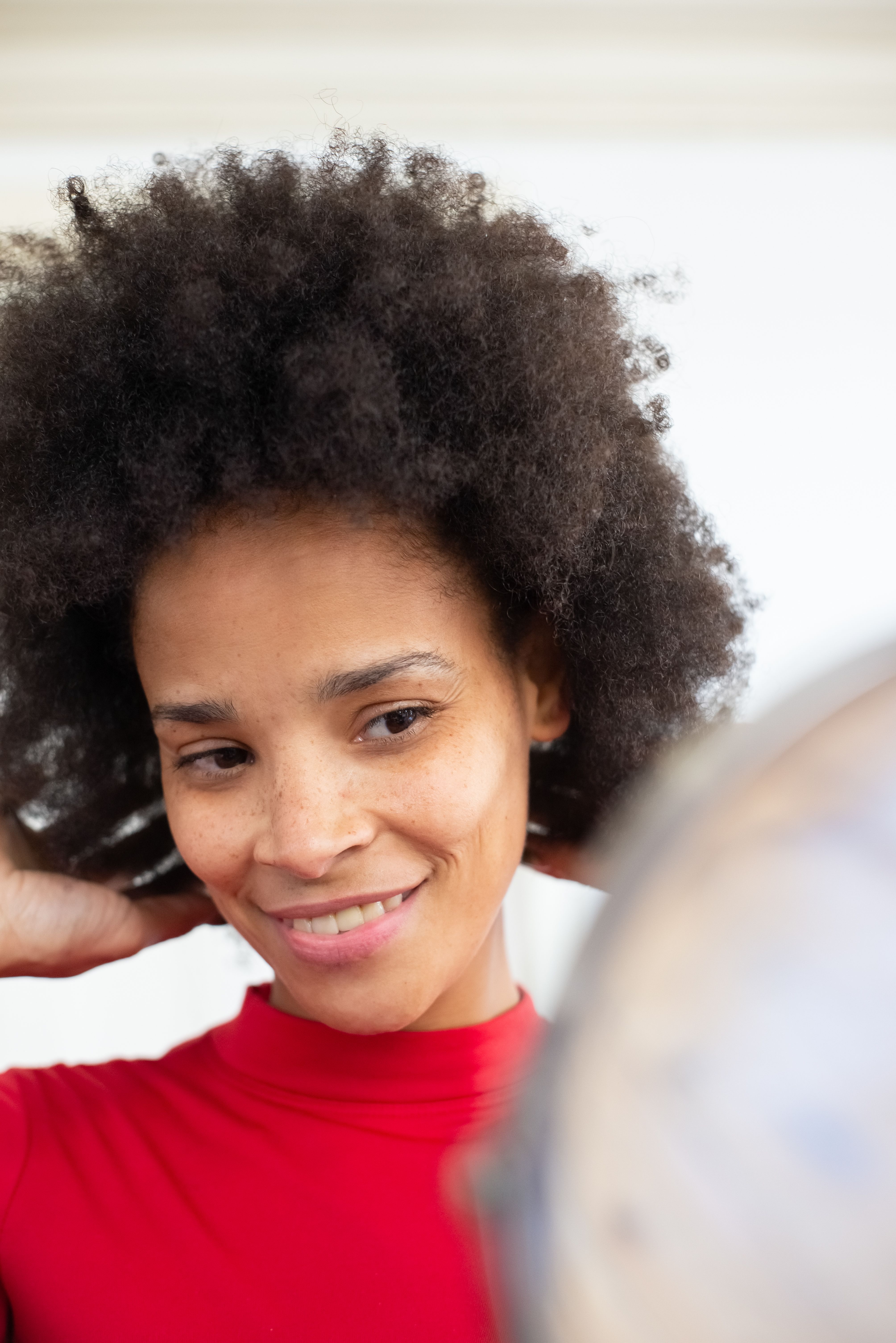 Portrait of a confident woman with afro hair, smiling as she adjusts her hairstyle, shot outdoors with natural lighting.