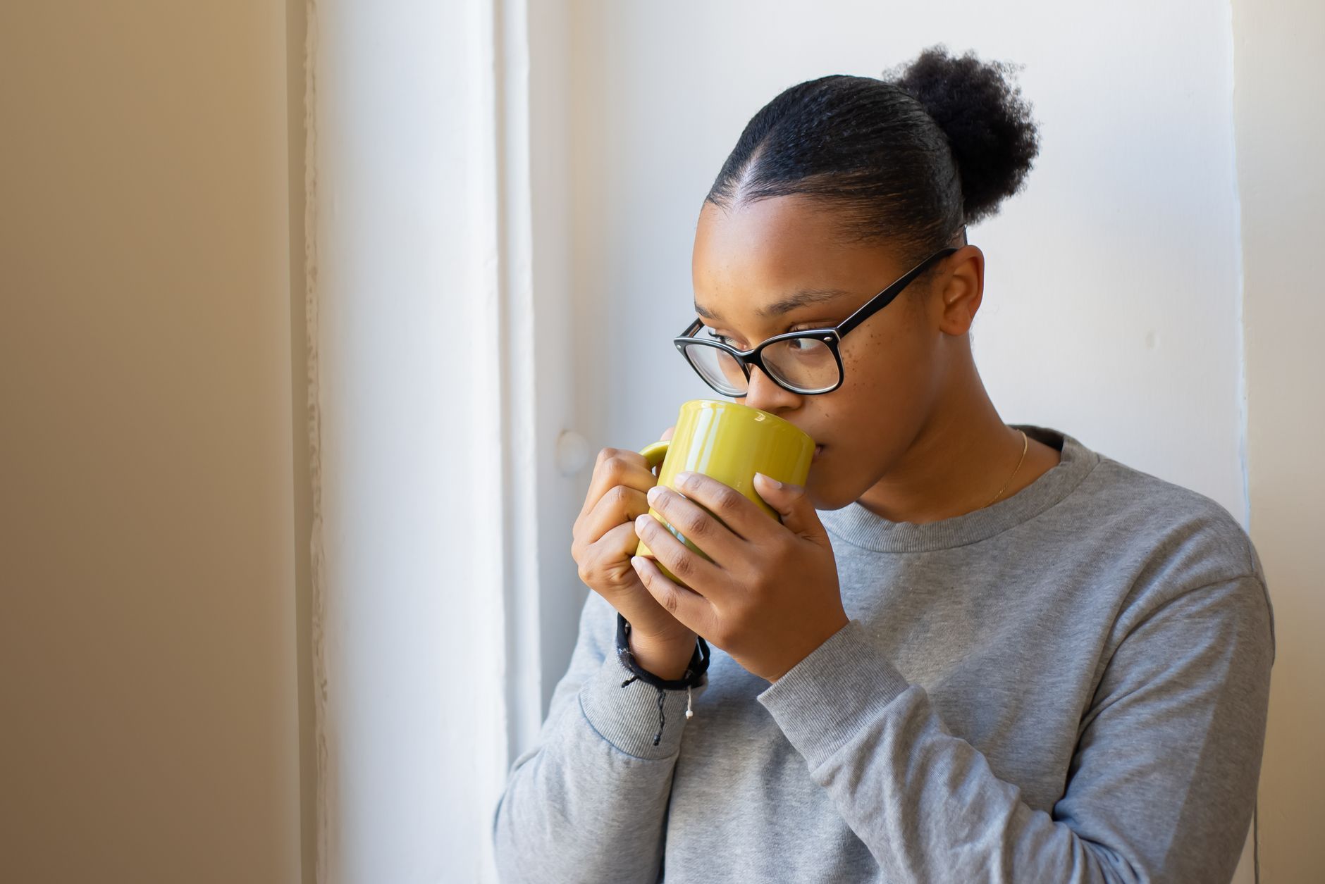 A woman in glasses calmly savoring a hot drink in a cozy indoor setting by a window.