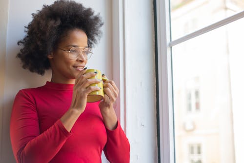 A Woman Holding a Cup while Looking Out the Window