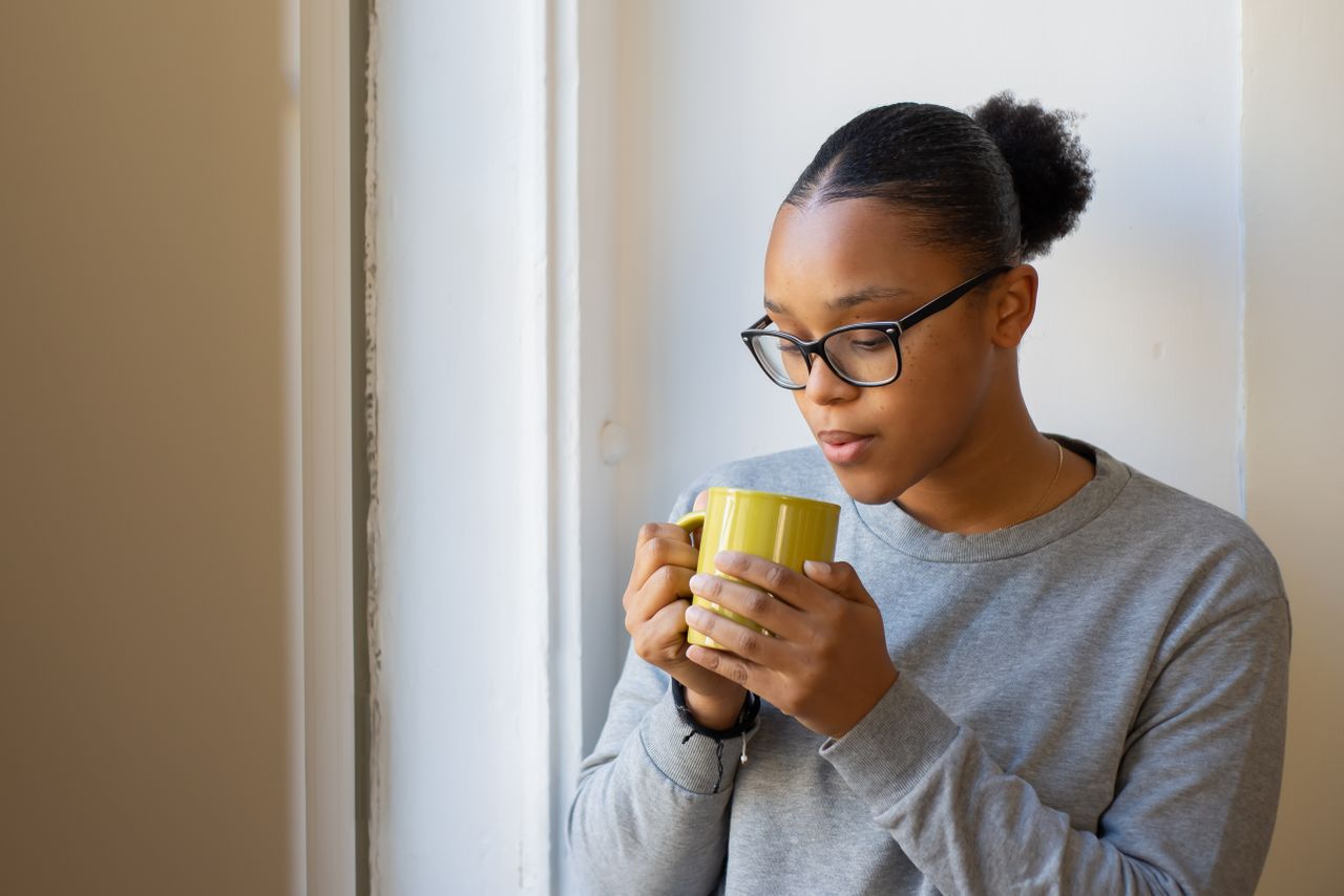 Woman with natural curly hair gathered in a high topknot holding a mug