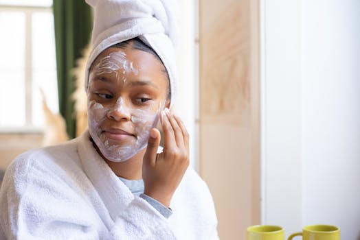 A young woman in a bathrobe applies face cream while relaxing indoors. Morning skincare routine.