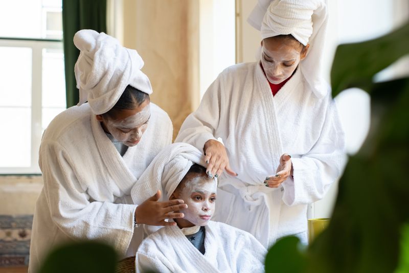 Women and a girl in white bathrobes applying facial cream at a spa party