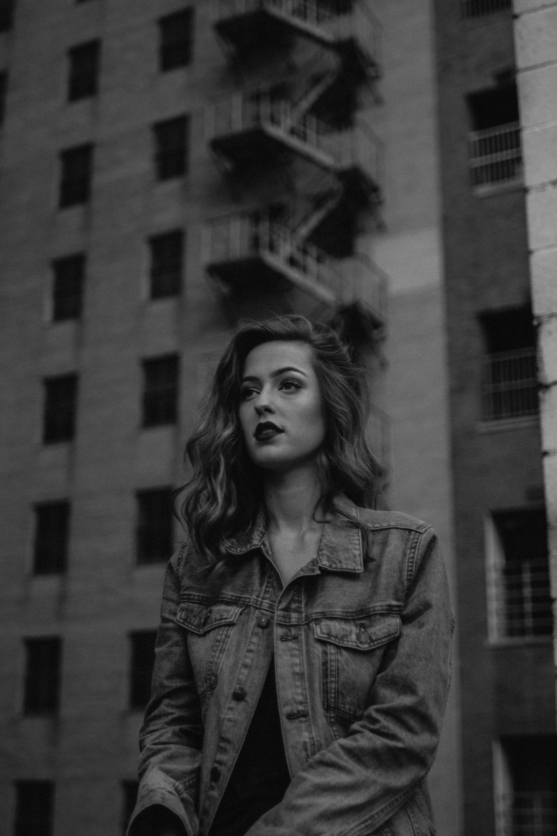 Monochrome portrait of a woman in a denim jacket against an urban backdrop.