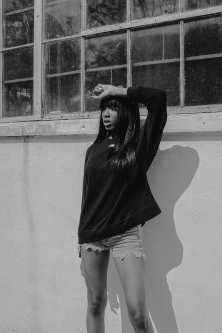 Monochrome portrait of a woman in casual attire striking a pose outdoors against a wall.