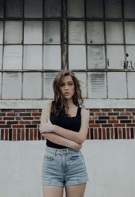 Stylish woman in casual outfit poses against a vintage industrial window. Urban and edgy look.