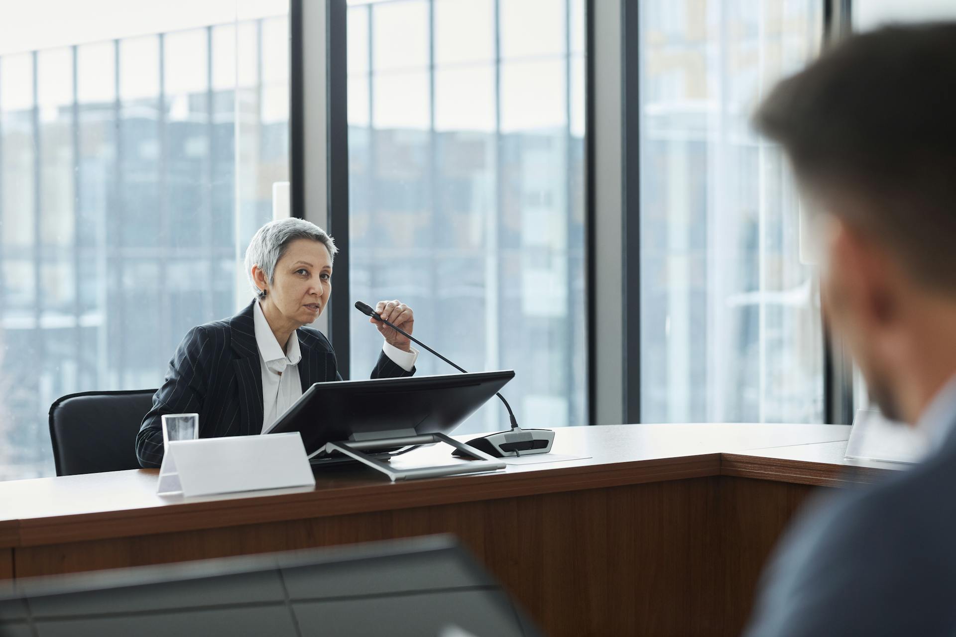 Businesswoman speaking at a corporate meeting in a modern office setting.